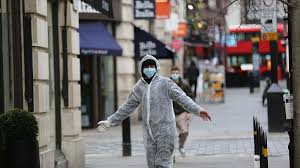 Person in a full-body protective suit walking down a mostly empty city street during a pandemic.